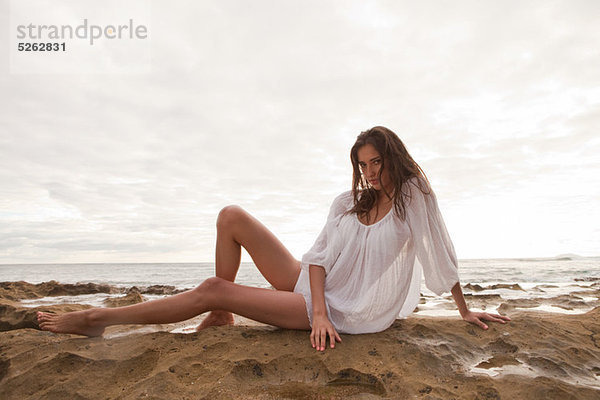 Young Woman wearing weiß oben sitzen auf Sand  Porträt