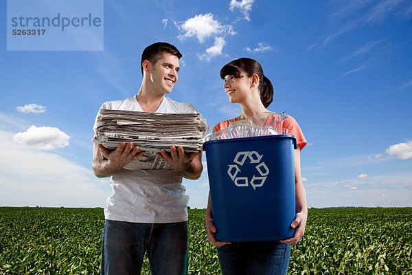 Paar im Feld Betrieb recycling und Haufen von Zeitungen