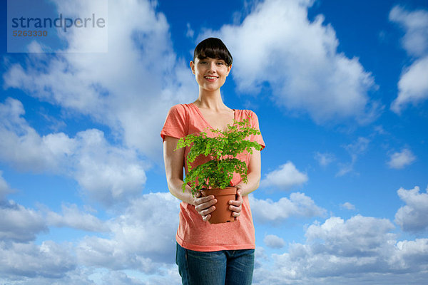 Young Woman holding Pflanze gegen blauen Himmel mit Wolken