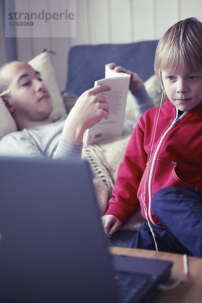 Boy wearing Kopfhörer Blick auf Laptopbildschirm  Mann im Hintergrund