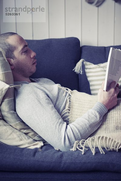 Mann liegt auf einer Couch und liest ein Buch