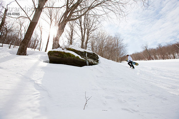 Junger Mann zu Fuß bergauf mit snowboard