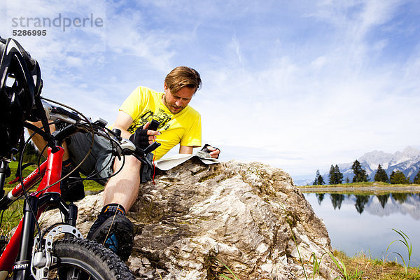 Mann mit Mountainbike an einem Felsen schaut in eine Landkarte