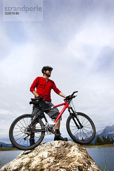 Mann mit Mountainbike auf einer Felsspitze