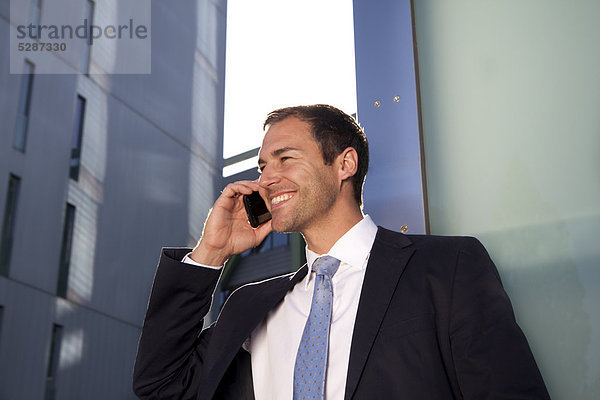 Lächelnder Geschäftsmann telefoniert mit Handy im Freien