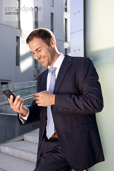 Lächelnder Geschäftsmann schaut auf Handy im Freien