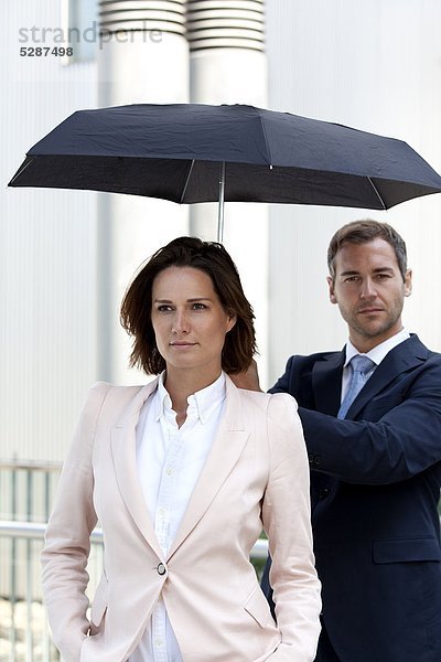 Geschäftsmann hält einen Regenschirm über einer Geschäftsfrau