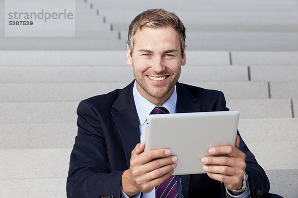 Geschäftsmann benutzt einen Tablet PC auf einer Treppe