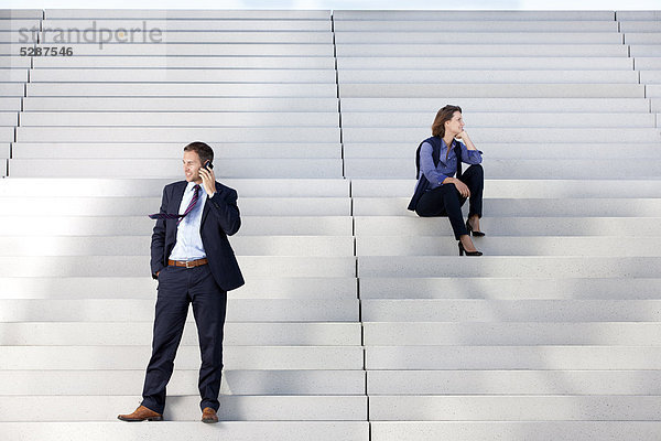 Geschäftsfrau und telefonierender Geschäftsmann auf einer Treppe