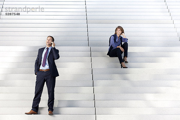 Geschäftsfrau schaut auf telefonierenden Geschäftsmann auf einer Treppe