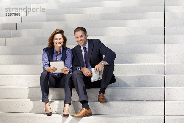 Geschäftsmann und Geschäftsfrau mit Tablet PC und Zeitung auf einer Treppe