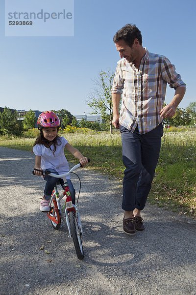 Vater rennt neben Tochter auf Fahrrad