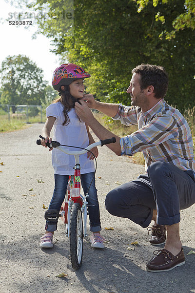 Vater schließt den Helm seiner Tochter auf dem Fahrrad