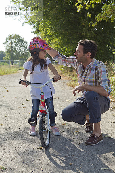 Vater und Tochter mit Helm auf Fahrrad im Freien