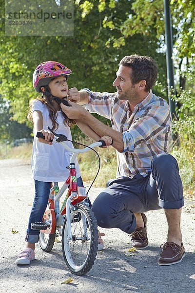 Vater schließt den Helm seiner Tochter auf dem Fahrrad