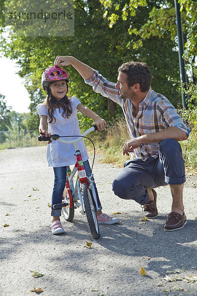 Vater und Tochter mit Helm auf Fahrrad im Freien