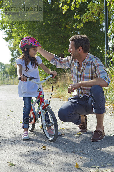 Vater und Tochter mit Helm auf Fahrrad im Freien