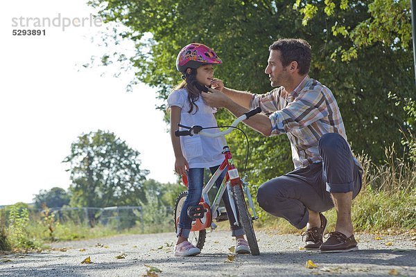 Vater schließt den Helm seiner Tochter auf dem Fahrrad