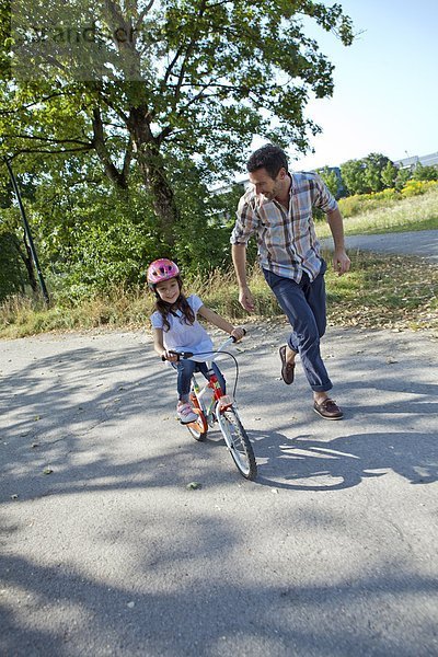 Vater rennt neben Tochter auf Fahrrad
