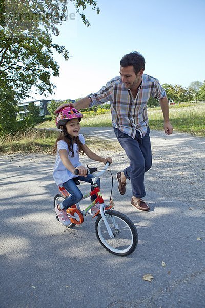 Vater rennt neben Tochter auf Fahrrad