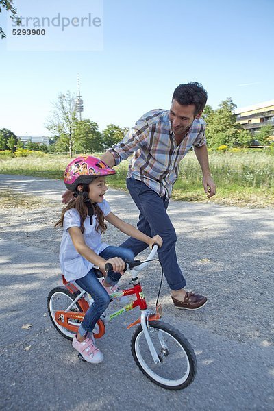 Vater rennt neben Tochter auf Fahrrad