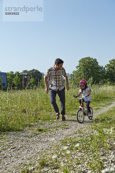 Vater rennt neben Tochter auf Fahrrad