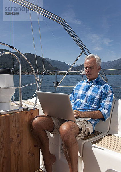 Älterer Mann mit Laptop auf dem Segelboot