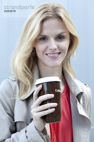 Lächelnde blonde Frau mit Coffee to Go