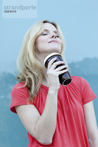 Lächelnde blonde Frau mit Coffee to Go