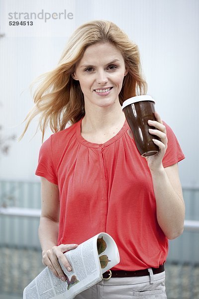 Lächelnde blonde Frau mit Coffee to Go und Zeitung