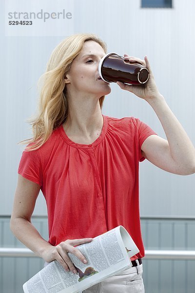 Blonde Frau mit Coffee to Go und Zeitung