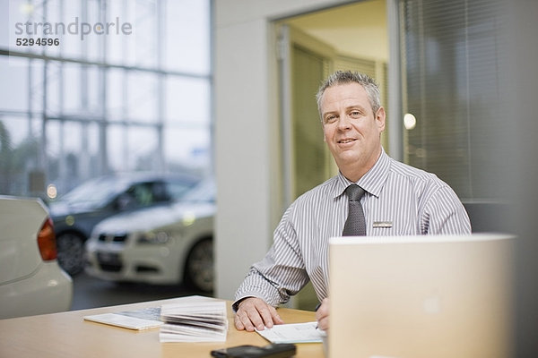 Autoverkäufer sitzend am Schreibtisch im Showroom