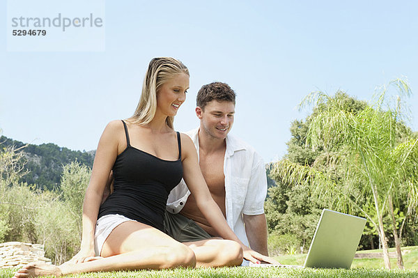 Paar mit Laptop im Gras zusammen