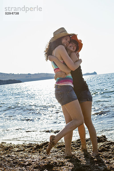 Frauen in Sonnenhüten umarmen sich am Strand
