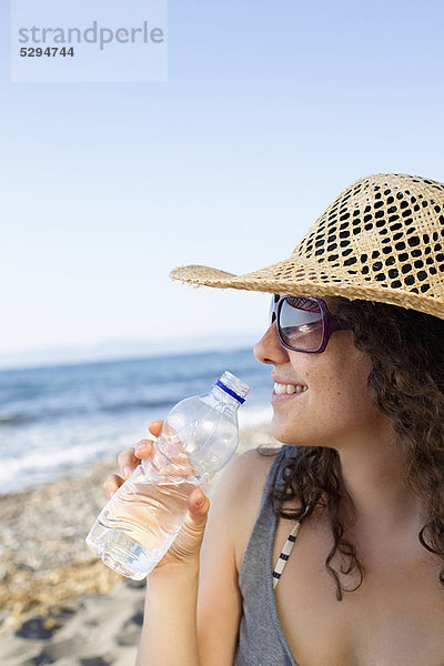 Lächelnde Frau trinkt Wasser am Strand