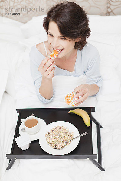 Lächelnde Frau beim Frühstück im Bett