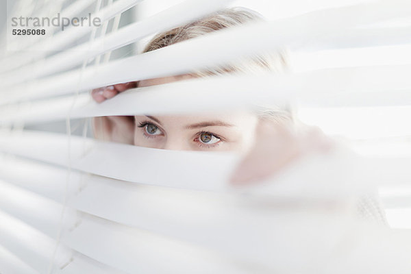 Teenager-Mädchen  das durch Jalousien schaut.