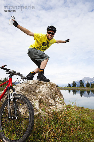 Mann mit Mountainbike posiert auf einer Felsspitze