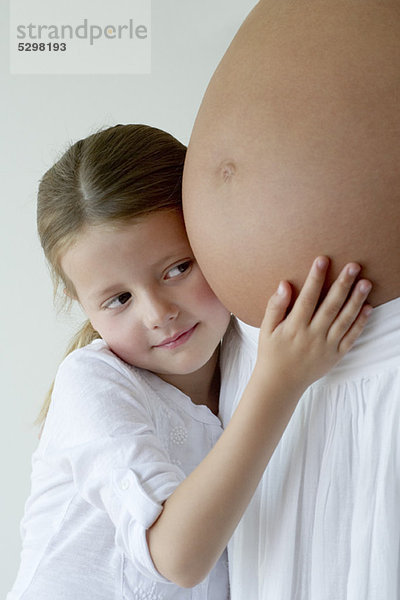 Mädchen  das den schwangeren Bauch der Mutter umarmt.