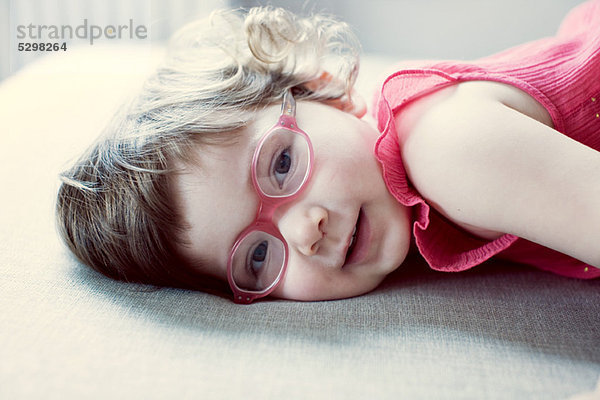 Kleines Mädchen mit Brille auf der Seite liegend