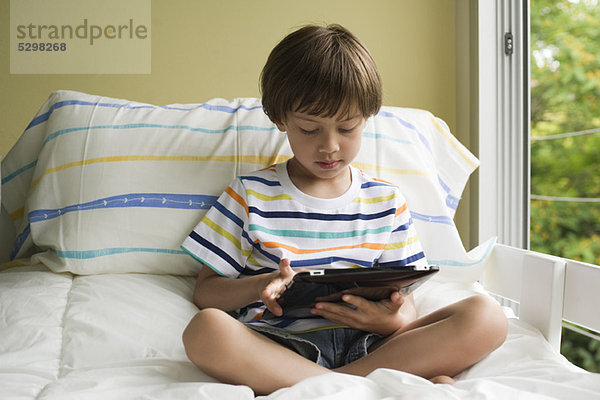 Junge auf dem Bett sitzend  mit digitalem Tablett
