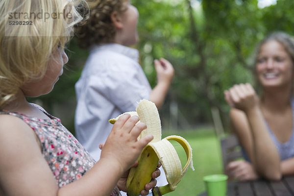 Kleines Mädchen im Freien mit ihrer Familie  das Banane isst.
