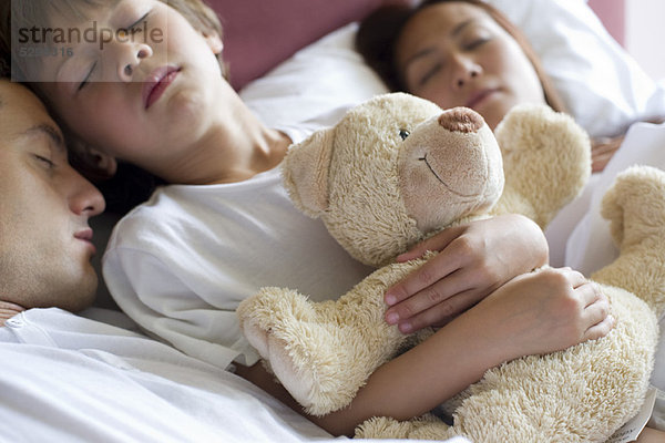 Junge schläft mit seinen Eltern im Bett  hält Teddybär in der Hand