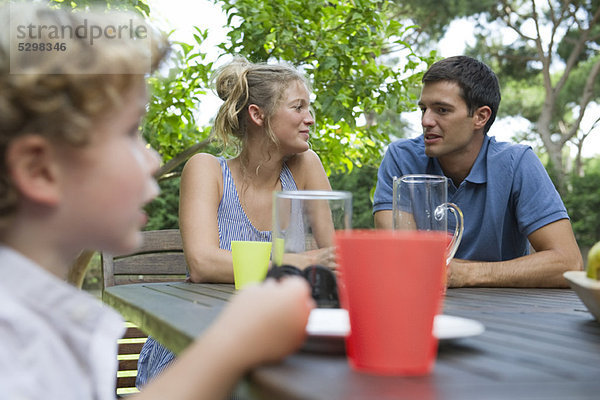 Familie entspannt gemeinsam am Tisch im Freien