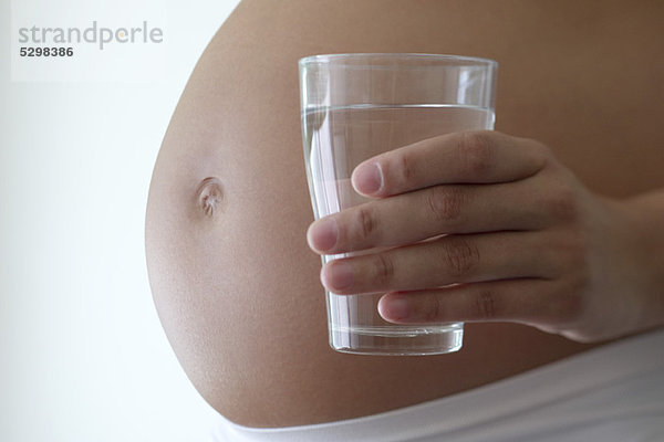 Frau hält ein Glas Wasser neben dem schwangeren Bauch  abgeschnitten