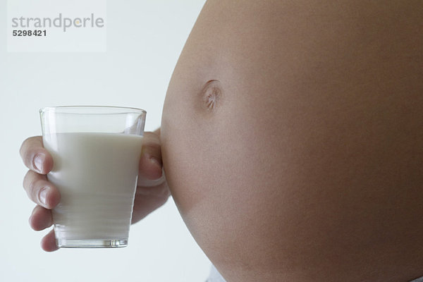 Frau hält ein Glas Milch neben dem schwangeren Bauch  abgeschnitten
