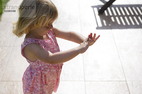 Kleines Mädchen  das im Freien steht und die Hände betrachtet.