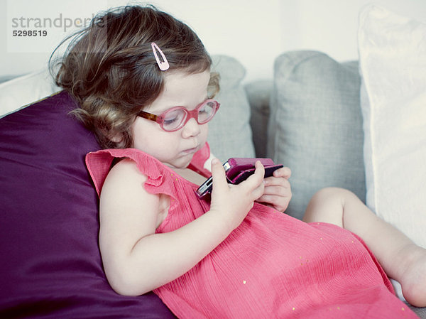 Kleines Mädchen liegt auf der Couch und schaut auf das Handy