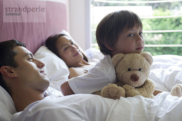 Junge im Bett mit seinen Eltern und seinem Teddybären