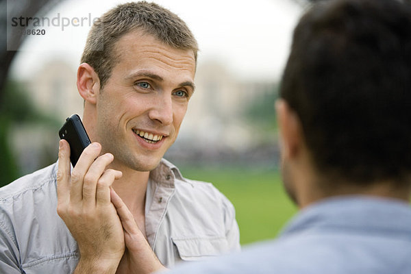 Mann am Telefon  der das Handy-Mundstück mit der Hand bedeckt  um mit Bekannten zu sprechen.